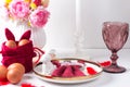 Romantic Easter table setting with candles, white plate, pink wine glass Table decoration with rabbit and painted eggs in red and