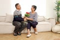 Romantic elderly man gives rose flower bouquet to his wife while sitting in living room, happy smiling Asian senior mature retired Royalty Free Stock Photo