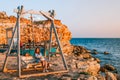 Romantic evening at sunset by the sea, a young woman in a dress with a bouquet of flowers is sitting on a wooden swing holding her Royalty Free Stock Photo