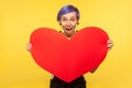 Romantic feelings. Portrait of surprised hipster girl holding big paper heart and looking with amazed eyes. yellow background