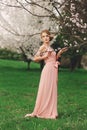 Romantic full height portrait of a young blonde woman in pink dress standing near the blooming cherry tree Royalty Free Stock Photo