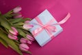 Romantic gift box tied with big pink bow and spring tulips on pink color background. Mother's day or Easter holiday Royalty Free Stock Photo