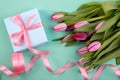 Romantic gift box tied with big pink bow and spring tulips on turquoise color background. Mother`s day or Easter holiday concept Royalty Free Stock Photo