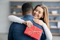 Romantic Gift. Grateful Girlfriend Hugging Her Black Boyfriend And Holding Present Box