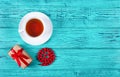 Romantic gift with red bow and cup of tea on wooden background. Gift for woman`s day. White cup of tea. Royalty Free Stock Photo