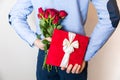 Valentines day gift surprise,man hiding gift and holding red rose bouquet