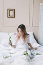 Romantic girl. Portrait of a girl in bed with natural flowers. Dreamy young woman with pink tulips resting in bedroom in morning Royalty Free Stock Photo