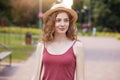 Romantic girl wearing straw hat and burgundy t shirt posing in park, looking smiling aside, enjoing beautiful nature. Adorable Royalty Free Stock Photo