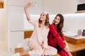 Romantic girls sitting on wooden table together and taking picture of themselves. Indoor shot of lovely ladies in