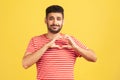 Romantic handsome bearded man in striped red t-shirt showing heart gesture with fingers, confessing love, showing his feelings