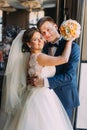 Romantic happy couple, groom embracing his bride near window closeup