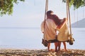 Affectionate couple sitting together on the beach on swing, silhouette of man hugging woman Royalty Free Stock Photo