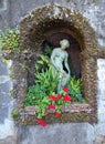 Romantic idyllic stone grotto in an antique style tropical garden with a delicate sculpture of female statue and vibrant red Royalty Free Stock Photo