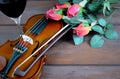 Romantic image of a violin with a glass of red wine and red roses on a rustic wooden table.