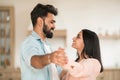 Romantic indian couple enjoying time together at home, dancing waltz, holding hands and smiling to each other