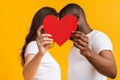 Romantic interracial couple kissing behind big red paper heart Royalty Free Stock Photo