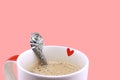 small red heart inside edge of white ceramic coffee cup and rose flower shaped metal silver spoon isolated on pink background Royalty Free Stock Photo