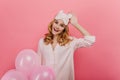 Romantic laughing girl touching her sleepmask and holding bright balloons. Indoor portrait of wonderful curly lady