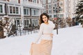 Romantic long-haired girl in skirt posing on the street full of snow with lantern on background. Outdoor portrait of