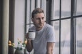 Romantic long-haired man drinking his morning coffee near the window