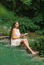 A romantic long-haired young woman with bare feet sits on a staircase in the open air and reads a book