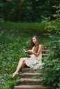Romantic long-haired young woman with bare feet sits on a staircase in the open air and reads a book