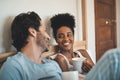 Romantic, loving and happy interracial couple having a cup of coffee on a bed in the morning at home. People in love Royalty Free Stock Photo
