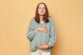 Romantic loving pregnant woman future mother wearing knitted warm sweater standing isolated over beige background sending air
