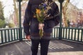 Romantic Man With Bouquet Of Flowers Behind Back Surprising Young Woman As They Meet In City Park