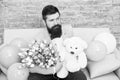 Romantic man with flowers and teddy bear sit on couch with air balloons waiting girlfriend. Romantic gift. Macho ready