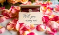 A romantic marriage proposal setup with a diamond engagement ring in a box surrounded by soft pink rose petals and a Will you Royalty Free Stock Photo