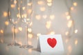 Romantic message note with red 3d heart on it, and champagne with glasses and fairy light strings with heart bokeh in the backgrou