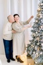 Romantic middle aged couple in love spending time together, while decorating Christmas tree. Hansome man kissing his