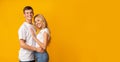 Romantic millennial guy and girl cuddling over yellow background