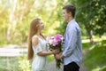 Romantic millennial guy presenting bouquet of beautiful flowers to his girlfriend in park