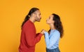 Romantic millennial man and woman kissing on orange background