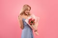 Romantic millennial woman in spring dress holding bouquet of tulips on pink studio background