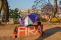 A romantic moment at the park, young couple sits under a purple umbrella on a cement bench with a word Fira,translates Unity