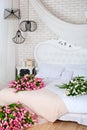 Romantic morning in a chic bedroom. A large bouquet of pink tulips lie on a white bed. Classic bedroom design. Brick white wall. M
