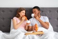 Romantic multiracial couple eating fresh croissants wth coffee, having breakfast in bed at home Royalty Free Stock Photo