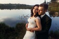 Romantic newlywed couple hugging near blue lake, sensual groom embracing gorgeous bride from behind near river, castle in the Royalty Free Stock Photo