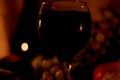 Romantic evening background with two candles flames reflection in a glass full of red wine with dark shades on grapes