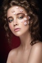 Romantic nude young beautiful girl with white flowers on her face and soft curls on dark background.