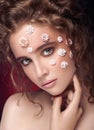 Romantic nude young beautiful girl with white flowers on her face and soft curls on dark background.