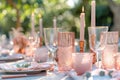 Romantic outdoor dinner setting features white tablecloth with pink and white glassware, pink napkin, and lit candle holder. Soft Royalty Free Stock Photo