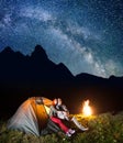 Romantic pair lovers looking to the shines starry sky and Milky way in the camping at night near campfire