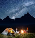 Romantic pair tourists sitting by campfire and tent under incredibly beautiful starry sky and looking to each other