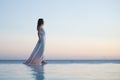 Romantic photo of graceful woman walking in flowing dress along the water edge