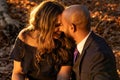 Romantic photo of a well dressed mixed race couple hugging and holding kissing each other at sunset in a city park
