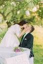 Romantic picknick in park. Playful bride kissng her lovely new husband while he sits at table